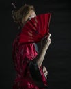 Western blonde woman dressed in oriental style hides part of her face behind a red fan Royalty Free Stock Photo