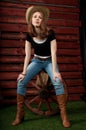 Western girl in cowboy hat sitts on wagon wooden wheel. Royalty Free Stock Photo
