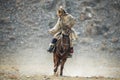 Western Mongolia.Traditional Golden Eagle Festival. Unknown Mongolian Hunter In Traditional Clothes Of Wolf Fur Astride On Brown Royalty Free Stock Photo