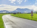 Wet asphalt road after rain at the countryside with road signs, green grass around and mountains on the horizon Royalty Free Stock Photo
