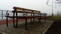 Wet bench on a foggy day. Metal curled wrought iron fence detail. Off-season melancholic mood Royalty Free Stock Photo