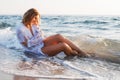 Wet blonde girl in white shirt  sitting in the water on the sea beach and looks at the   the dawn of the sun. Concept: summer Royalty Free Stock Photo