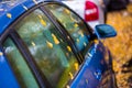 Wet blue car side with autumn leaves and selective focus