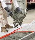 Wet cement off loaded by hands of a construction worker from a cement truck chute into a concrete form made of wood