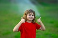 Wet child face. Kid play in garden near irrigation watering sprinkler system. Watering grass with automatic sprinkler Royalty Free Stock Photo