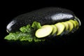 Wet courgettes cut into slices and leaves on black Royalty Free Stock Photo