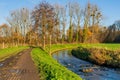 Wet dirt path next to a stream with its waters flowing between stones surrounded by green grass, bare trees and farm fences Royalty Free Stock Photo