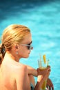 Wet girl emerged from the water drinks orange fresh by the pool.