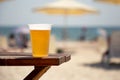 Wet glass of golden cool tasty beer on the wooden table on the shore of the sea or ocean on the sunset. Concept of beach