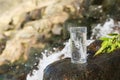 Wet glass of water on rocks near flowing stream outdoors, space for text Royalty Free Stock Photo