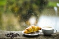 Wet glass window and cup of hot caffeine beverage. Coffee drink with croissant dessert. Enjoying coffee on rainy day Royalty Free Stock Photo