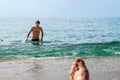 A wet, handsome dark-haired man emerges from the water on a Mediterranean beach in Alanya, Turkey. Blurred female foot against the