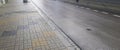 A wet pavement stretches alongside an empty road. The scene captures the reflection of the grey sky on the wet surface, Royalty Free Stock Photo