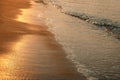 Wet sand with glittering sea wave at the beach in the light of setting sun. The sun's light is reflecting like a golden Royalty Free Stock Photo