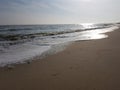 Wet sandy beach and sea with small foam waves, solar track on the water, autumn sunny day Royalty Free Stock Photo