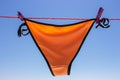 Wet swimsuit on the rope with pins on the beach. Orange bikini bottom drying on clothesline on blue sky background. Summer fashion