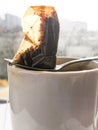 Wet used disposable tea bag on a metal spoon lying on a white dirty ceramic cup in the backlight from the window Royalty Free Stock Photo