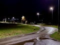 Wet Winding Road at Night Illuminated by Street Lamps with Rural Houses in Background Royalty Free Stock Photo