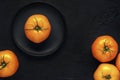 Wet yellow tomato fruit in black plate and a few fruits on a dark textured background. Top view. Space for text Royalty Free Stock Photo