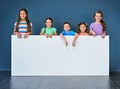 Weve got a message for you. Studio shot of a diverse group of kids standing behind a large blank banner against a blue Royalty Free Stock Photo