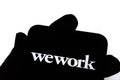 WeWork logo on the smartphone hold by a silhouette of a hand in front of white screen