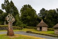 View of an early reconstructed Christian monastery in the Irish National Heritage Park with a large Celtic cross in the foreground