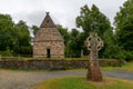 View of an early reconstructed Christian monastery in the Irish National Heritage Park with a large Celtic cross in the foreground