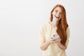 What beautiful day to chat online. Indoor shot of emotive happy redhead woman holding smartphone, gazing at camera Royalty Free Stock Photo