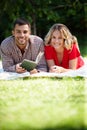 What better way to relax together...a happy young couple reading a book while lying on the grass in a park. Royalty Free Stock Photo