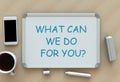 WHAT CAN WE DO FOR YOU?, message on whiteboard, smart phone and coffee on table