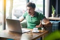 What do you want? Young angry businessman in green t-shirt sitting, working, looking and screaming at laptop screen on video call