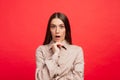 What is it. The female portrait isolated on red studio backgroud. The young emotional angry, scared woman looking at camera.The