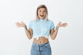 What great surprise. Portrait of happy emotive young woman with fair hair tattoos and pierced belly, smiling broadly and