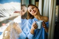 Portrait of a joyful young woman enjoying a cup of coffee at home. Smiling beautiful girl drinks hot tea in winter. Royalty Free Stock Photo
