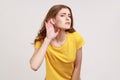 What? I can`t hear! Portrait of girl in yellow T-shirt holding hand near ear and listening carefully, having hearing problems,