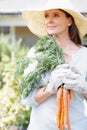 What is life without vegetables. A beautiful woman, wearing gardening gloves and a straw hat, holds a bunch of carrots Royalty Free Stock Photo