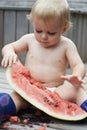 What a mess. A toddler sitting outside playing with a watermelon slice and making a big mess.
