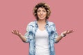 What? Portrait of confused or shocked young woman with curly hairstyle in casual blue shirt standing with raised arms and looking