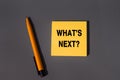 What`s Next - words written in a sticky note. Closeup of a personal agenda. Orange square sticky note and pen on grey background, Royalty Free Stock Photo