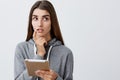 What should I buy. Close up of charming good-looking young caucasian girl with dark long hair in casual grey hoodie