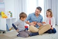 What song should I play for you guys. a happy father playing the guitar for his son and daughter at home. Royalty Free Stock Photo