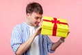 What is there? Portrait of curious happy brown-haired man unpacking present. indoor studio shot isolated on pink background