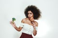 What to choose Frustrated afro american woman is facing a choice of healthy broccoli or sweet lollipop and looking at