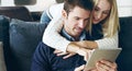 What you looking at. Cropped shot of an affectionate young couple using a digital tablet while sitting on their sofa at Royalty Free Stock Photo