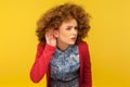 What are you saying? Portrait of woman with curly hair holding hand near ear and listening carefully