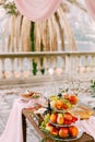 Whatnot for fruit with three tiers with apples, grapes, and pears on a table in the yard near the fence with columns.