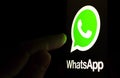 WhatsApp logo on the smartphone screen in a dark room and a finger pointing at it