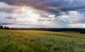 Wheat agriculture field with trees and distant hill, cloudy sky, rainbow and sun. Czech summer landscape Royalty Free Stock Photo