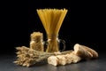 Wheat bunch, baguette, macaroni and pasta in jar, on black background. Grain bouquet and bread on dark wooden table. Gold