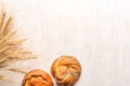 Wheat ears and fresh buns on white wooden background